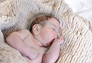 Cute little baby boy or girl,Â on soft beige plaid, sucking his finger